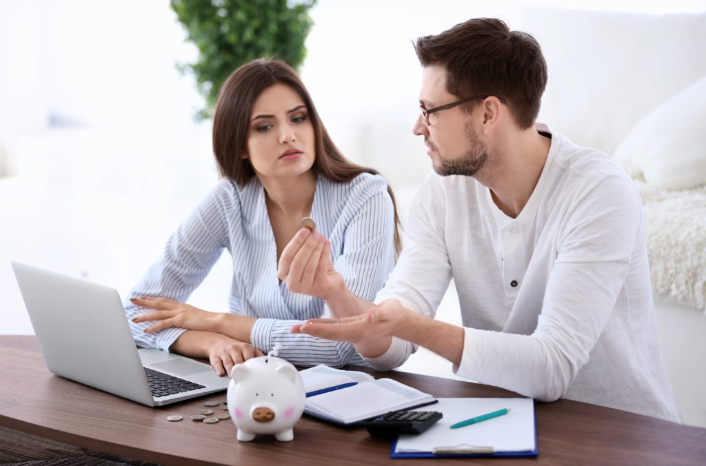 A man and a women sitting in front of a laptop in their living room discussing their finances
