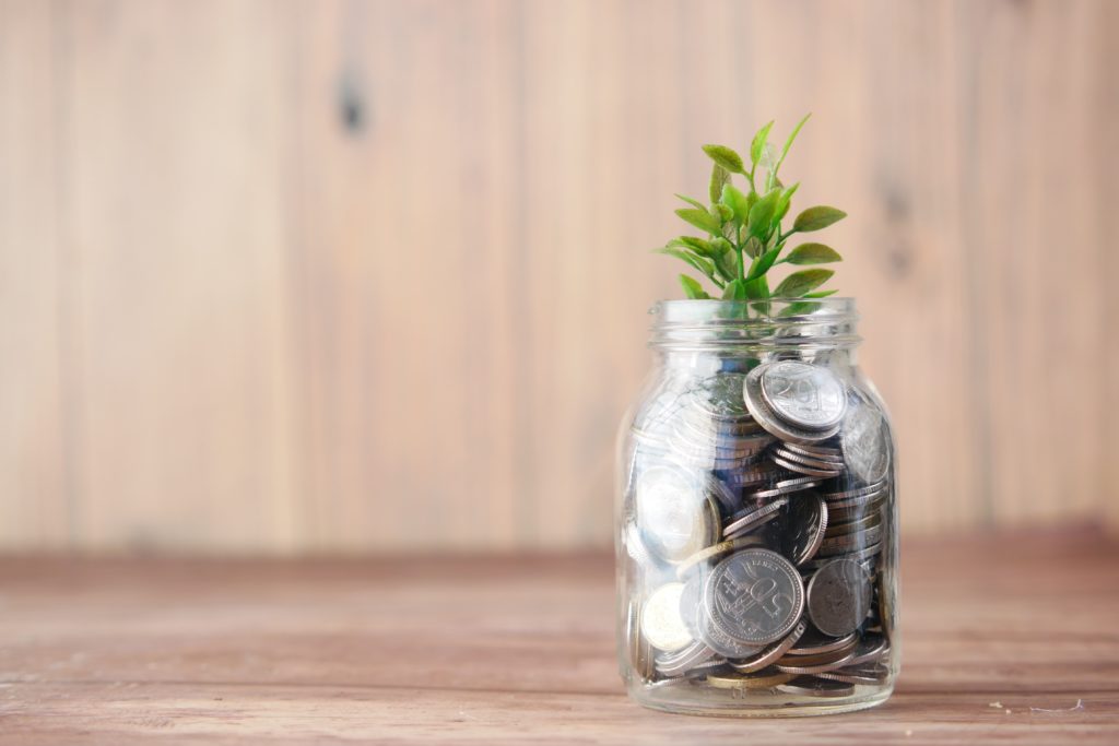 A jar on a table representing an investment concept with plant growing through coins