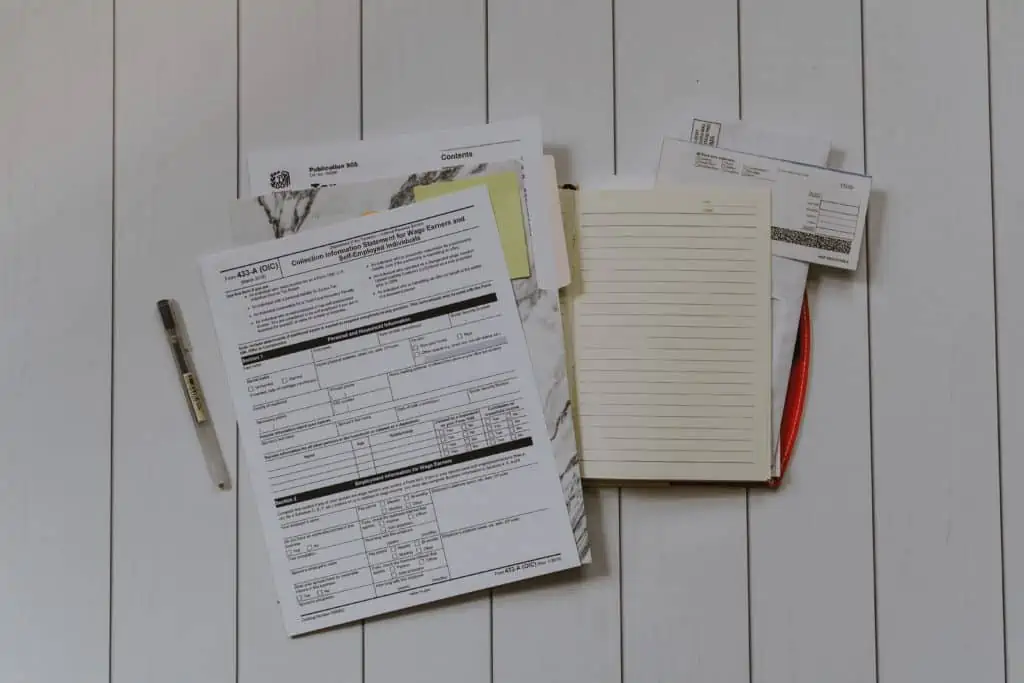 A stack of financial documents, forms, and a lined notebook on a wood panel table