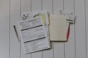 A stack of financial documents, forms, and a lined notebook on a wood panel table