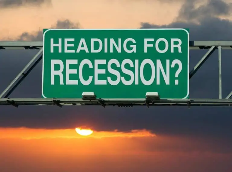 Overhead interstate sign that says Heading for recession? with a sunset in the background