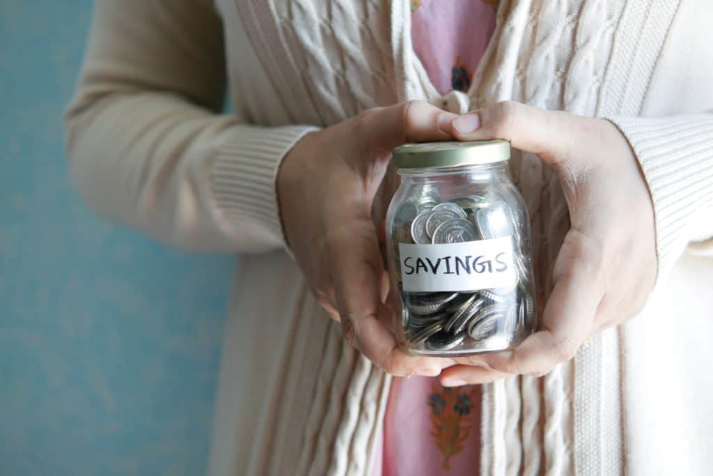 Close up of a woman holding a jar full of coins that is labeled Savings