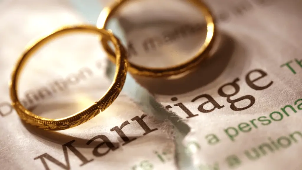 Close up of two rings sitting on top of a dictionary definition of Marriage ripped down the middle