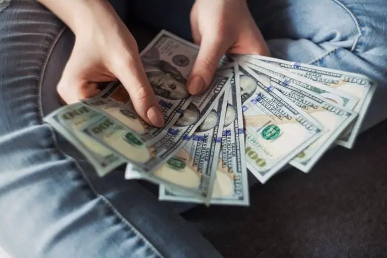 Woman sititng on the floor fanning out $900 in $100 bills
