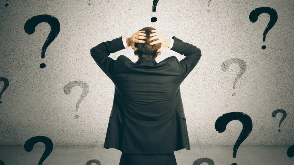 Man in a suit grasping his head in confusion with question marks surrounding him
