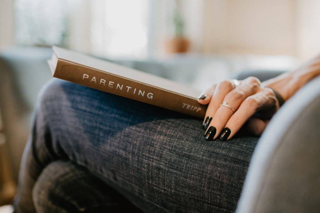 Close up shot of a book spine that is titled Parenting by Tripp resting on a woman's lap