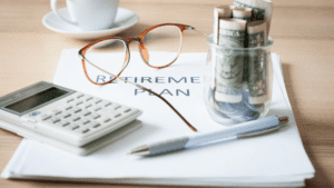Calculator, glasses, a pen, and a jar full of bills and coins sitting atop a document titled Retirement Plan